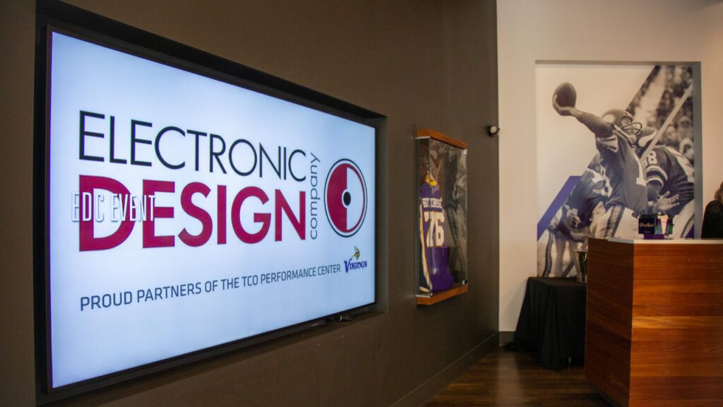 Image of a sports or athletic conference room. A glass case houses a Minnesota Vikings jersey. A large screen installed by Electronic Design Company fills one wall.