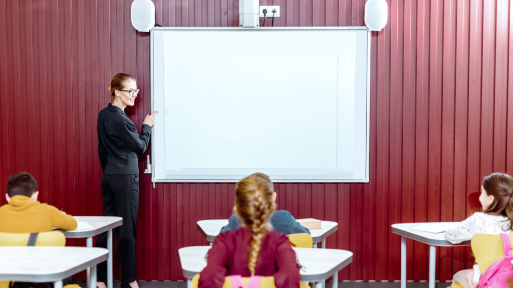 A teacher in a classroom uses a smart board to improve her students' education.