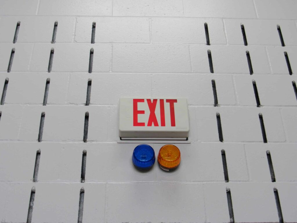 An exit sign, a blue emergency light and yellow emergency light serve as critical communication systems in an industrial setting.